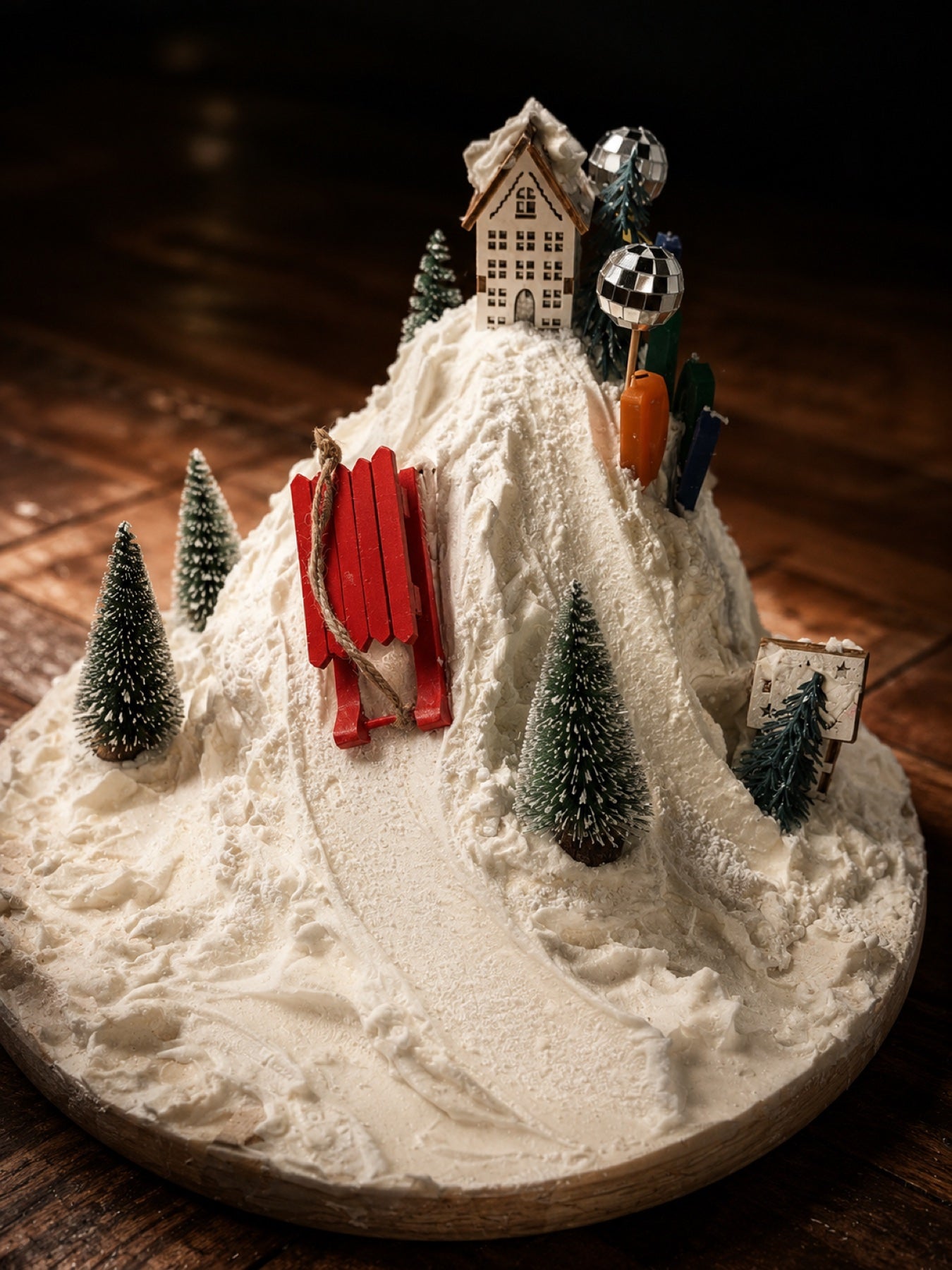 Sculptuurtaart als besneeuwde piste met chalet, dennenbomen en een rode slee